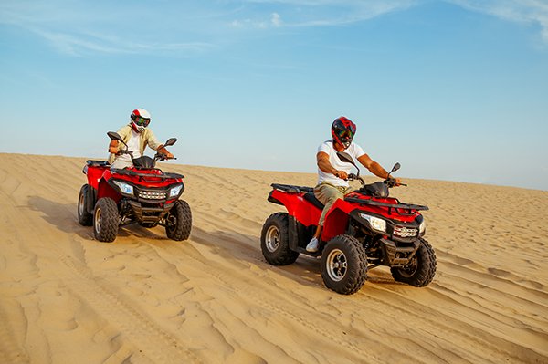 Two racers coming down from the dunes on atv Two racers coming down from the dunes on atv, desert sands. Male persons on quad bikes, sandy race, safari in hot sunny day, 4x4 extreme adventure, quad-biking